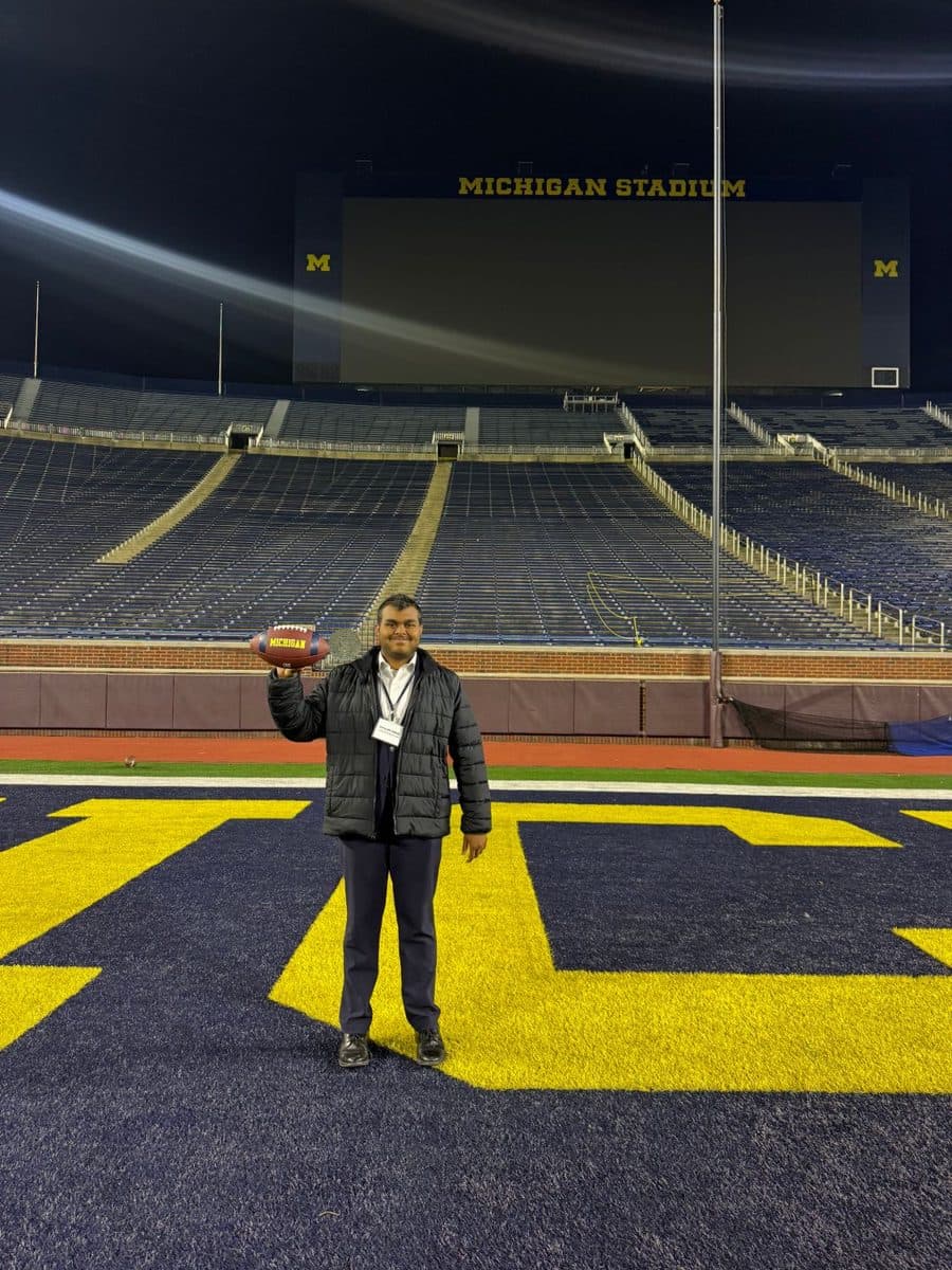 Vishanth holding a Michigan football in the end zone of Michigan Stadium at night