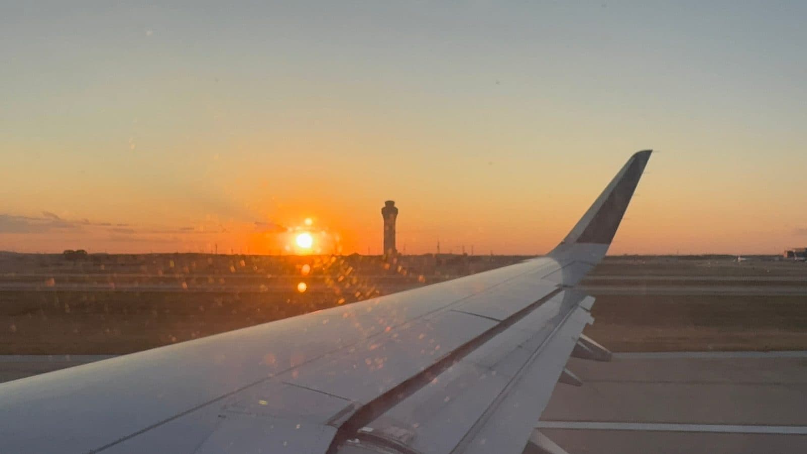 Airplane wing at sunset beside an airport control tower